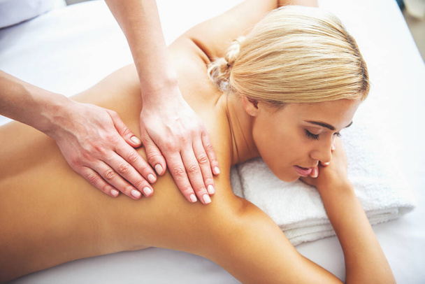 Bovenaanzicht van mooie blonde meisje liggend op de voorkant van haar lichaam, terwijl een massagetherapeut is haar rug masseren - Foto, afbeelding