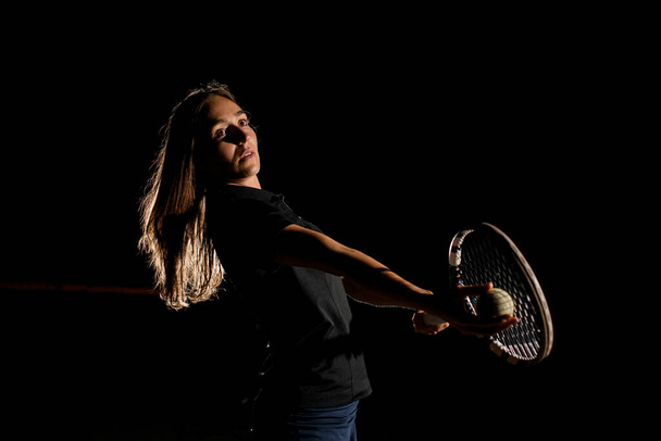 view on professional female tennis player holding in hand tennis ball and getting ready to serve. Dark background - Photo, image