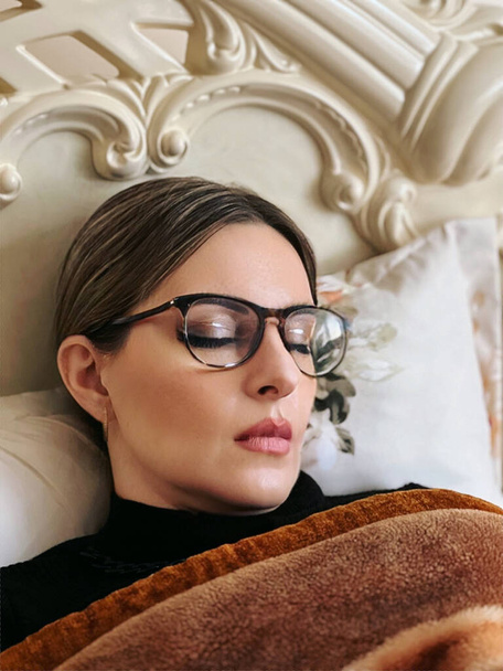 Молодая спящая женщина в очках лежит на кровати.. - Фото, изображение