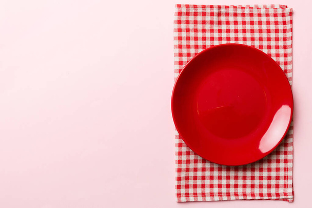 Visão superior sobre fundo colorido vazio redondo prato vermelho na toalha de mesa para alimentos. Prato vazio no guardanapo com espaço para o seu design. - Foto, Imagem