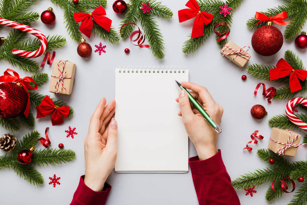 Kobieta pisząc Boże Narodzenie zrobić listę na notatniku na kolorowe tło z dekoracjami xmas. - Zdjęcie, obraz