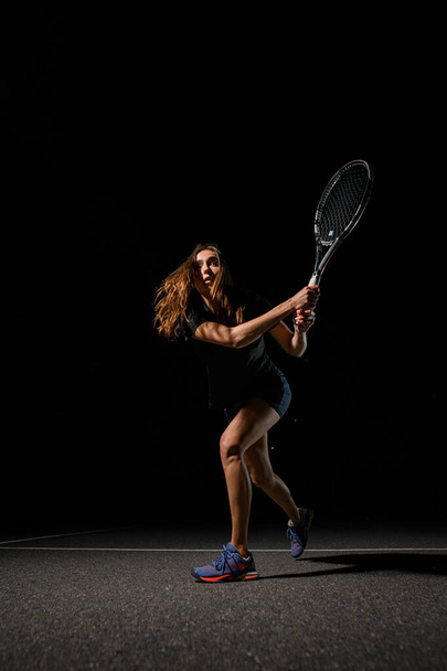 Great view of athletic woman tennis player with racket in special pose which preparing to playing tennis. Shot before to hitting tennis ball. Dark background - Foto, imagen