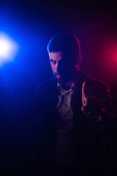 Photo of man posing on dark background with blue and pink lights. Concept of man showing fist. - 写真・画像