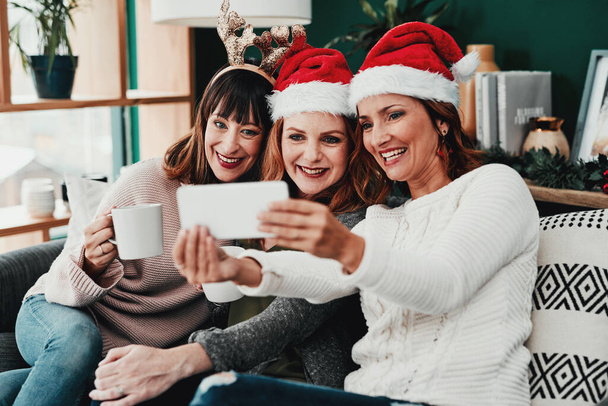 Τα πήγαμε καλά με τα κοστούμια. τρεις ελκυστικές μεσήλικες γυναίκες που παίρνουν αυτοπορτρέτα μαζί με ένα κινητό τηλέφωνο στο σπίτι κατά τη διάρκεια των Χριστουγέννων - Φωτογραφία, εικόνα
