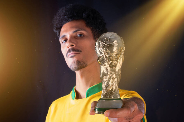 Giocatore di calcio brasiliano nero Holding vincitore del trofeo e celebrando, isolato su sfondo nero. - Foto, immagini