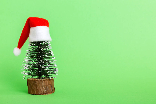 One small Christmas tree with santa hat on colored background. new year decoration with copy space. - Zdjęcie, obraz