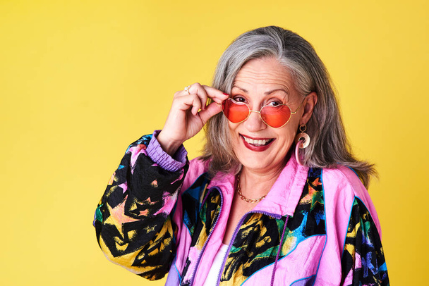 Věk je pocit, ne několik let. Portrét sebevědomé a stylové starší ženy, která nosí sluneční brýle pózující na žlutém pozadí - Fotografie, Obrázek