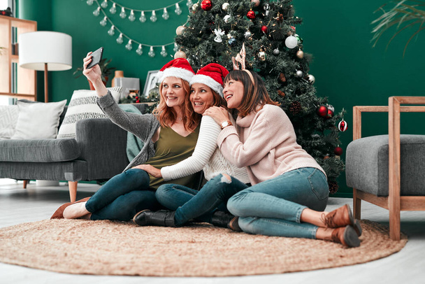An awesome Christmas card. three attractive women taking Christmas selfies together at home - Photo, Image