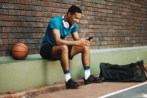 Man, basketball player or phone for social media app, health data analysis or motivation training schedule. Smile, happy or sports athlete on basketball court on mobile technology in exercise workout. - Фото, изображение