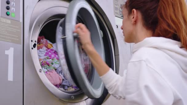 Ama de casa mujer joven hacer tareas domésticas, ocupado en el trabajo de limpieza regular poner toallas en la lavadora, enciende el moderno aparato de lavadora-secadora en el acogedor lavadero. Concepto de tareas domésticas. - Imágenes, Vídeo