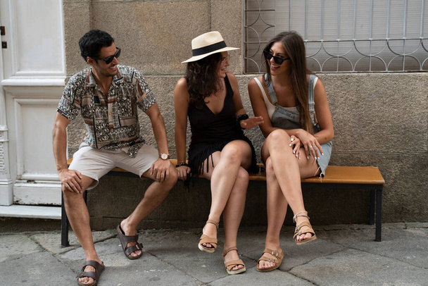 eine Gruppe von drei Freunden amüsiert sich und lacht auf einer Bank auf der Straße. Hochwertiges Foto - Foto, Bild