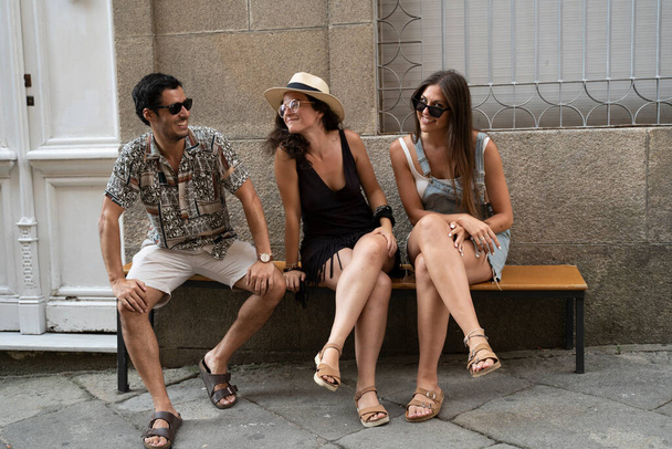 eine Gruppe von drei Freunden amüsiert sich und lacht auf einer Bank auf der Straße. Hochwertiges Foto - Foto, Bild