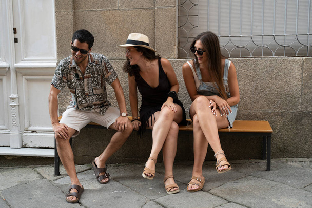 a group of three friends having fun and laughing on a bench in the street. High quality photo - Photo, Image