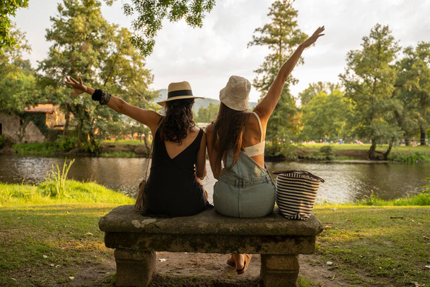Két kalapos barátnő, akik egy kőpadon ülnek a folyó előtt. Kiváló minőségű fénykép - Fotó, kép