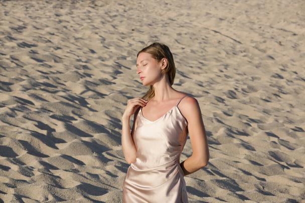 Krásný mladý model v béžovém hedvábí satén dlouhé šaty, módní letní portrét na pláži - Fotografie, Obrázek