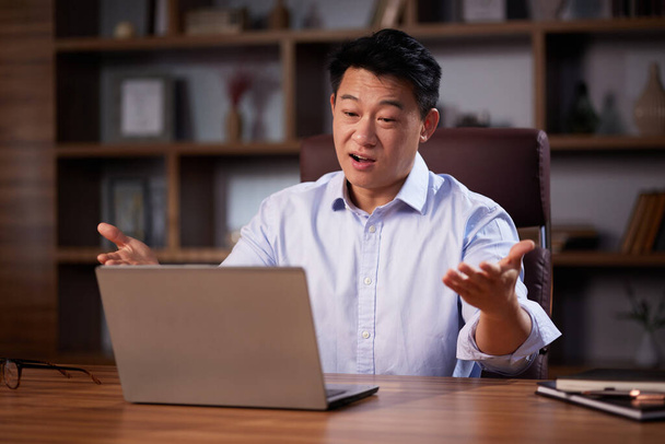 Asian man holding online webinar using laptop webcam, sitting in a home office. Man having online meeting and communicating remotely, looking at computer screen. - Photo, Image