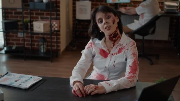 Horror zombi vigyorog hátborzongató irodai munkahelyen, miközben morog a kamera előtt. Agyhalott szörny mély és goromba sebekkel a munkahelyen ülve, gonosz és bizarr mosollyal.. - Felvétel, videó
