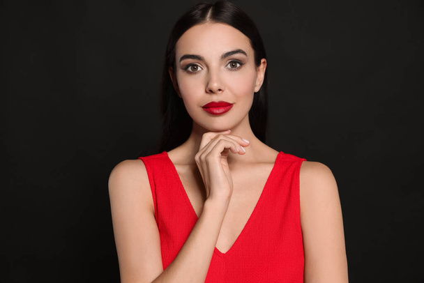 Portrait of young woman wearing beautiful red lipstick on black background - Фото, зображення