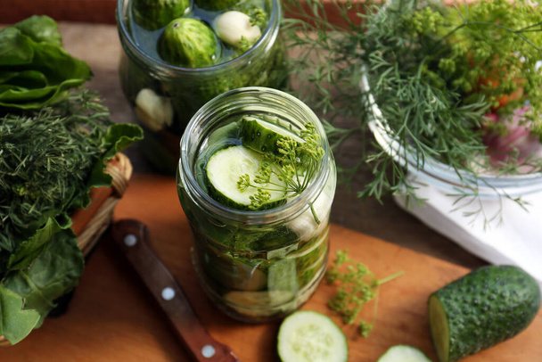 Glass jars, fresh cucumbers and herbs on wooden table. Pickling recipe - Foto, immagini