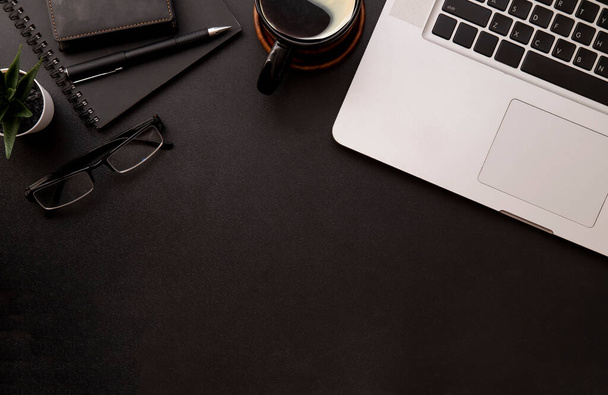 Laptop von oben, Brille, Notizbuch und Kaffeetasse auf schwarzem Schreibtisch. - Foto, Bild