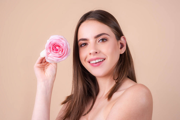 Portrait of attractive woman with pink rose on beige background. Portrait of a happy beautiful young girl with a pink rose in hands. Romance girl, romantic flowers. Beauty spring - Foto, Bild