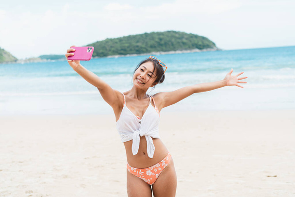 Portrait of happy smiling beautiful women taking a selfie photo on the beach. Pretty young Asian girl in casual looking clothes recording vlog video in bright sky - Photo, Image
