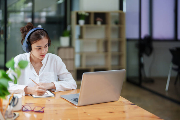 Portret pięknej kobiety korzystającej z komputera, słuchawki i notesu podczas wideokonferencji - Zdjęcie, obraz