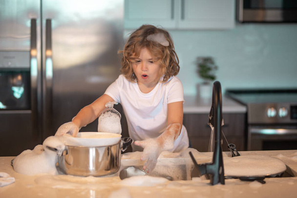 Funny twin boys helping in kitchen with washing dishes. Children having fun with housework. Child housekeeper washing the dishes on soapy water. Cute Funny boy washing dishes in kitchen - Photo, image