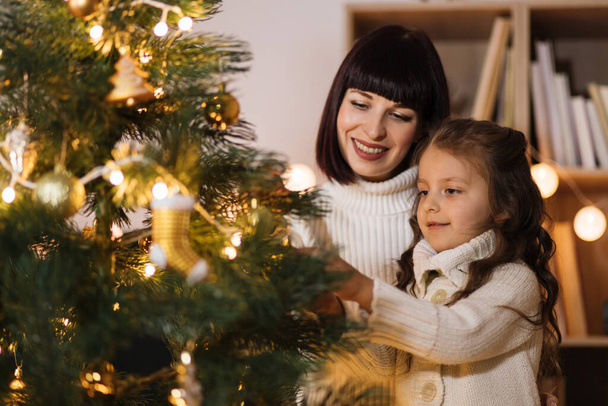 concept de famille, vacances d'hiver et personnes - mère heureuse et petite fille décorant l'arbre de Noël à la maison. - Photo, image