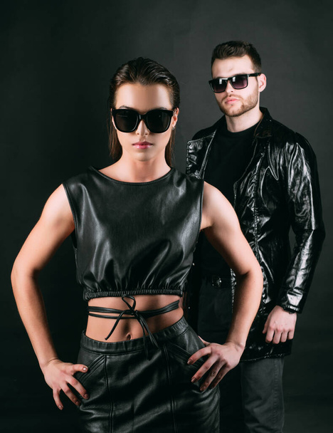 Couple in fashion black sunglasses. Young couple posing with sunglasses on black. Studio shot on dark background. Hipster boy and beauty girl. Vogue Style - Photo, image