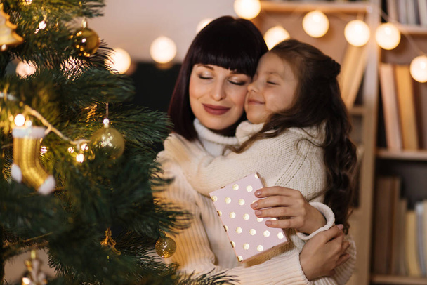Excited preschool girl, child celebrate New Year at home with loving young mother. Happy mom hugging small daughter with Christmas and congratulate her with gift. Celebration concept. - Photo, image