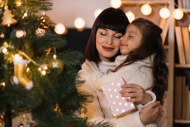 Excited preschool girl, child celebrate New Year at home with loving young mother. Happy mom hugging small daughter with Christmas and congratulate her with gift. Celebration concept. - Foto, Bild