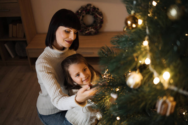 Mother and daughter decorating Christmas tree at home. Stylish interior of a childrens room. Scandinavian eco-style decor. New Year celebration. Christmas eve. Support joint time forwarding. Love - Valokuva, kuva