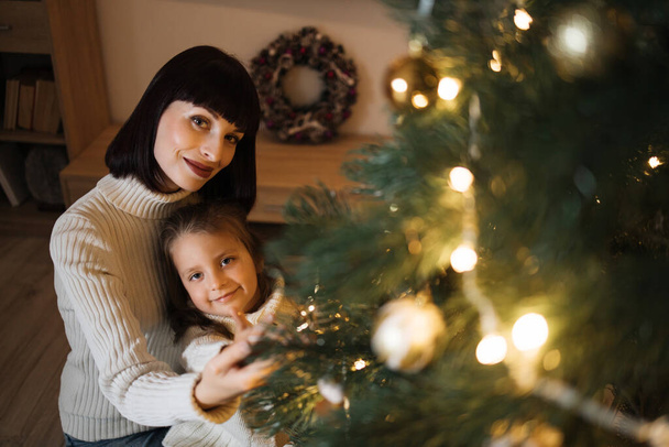 Mother and daughter decorating Christmas tree at home. Stylish interior of a childrens room. Scandinavian eco-style decor. New Year celebration. Christmas eve. Support joint time forwarding. Love - Photo, Image