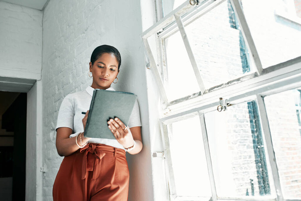 Getting it all done with one device. a young businesswoman using a digital tablet in an office - Foto, imagen