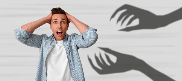 Scared man having panic attack and monster hands on light background - Photo, Image