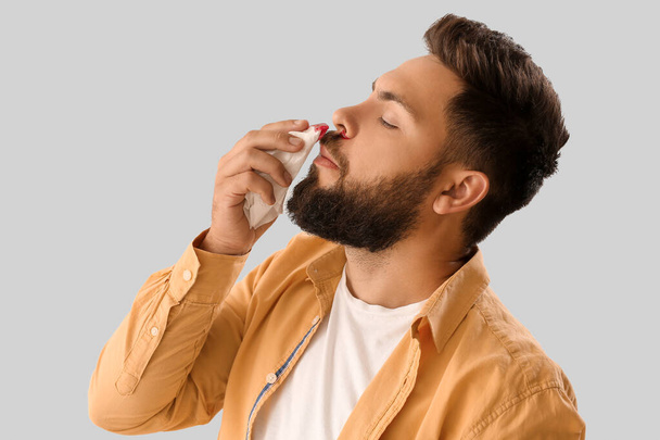 Young bearded man with nosebleed and tissue on light background, closeup - Photo, Image