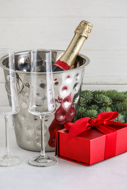 Vödör üveg pezsgő, szemüveg, karácsonyi ajándék és fenyő ágak fehér fa háttér - Fotó, kép
