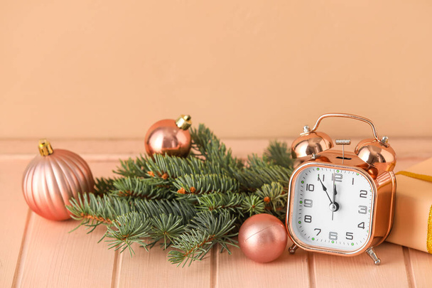 Alarm clock with Christmas balls, fir branches and gift on beige wooden background - Photo, Image
