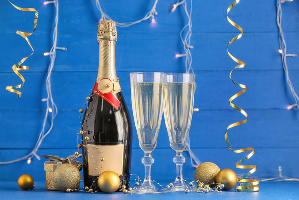 Bottle, glasses of champagne and Christmas decorations on color wooden background - Фото, изображение
