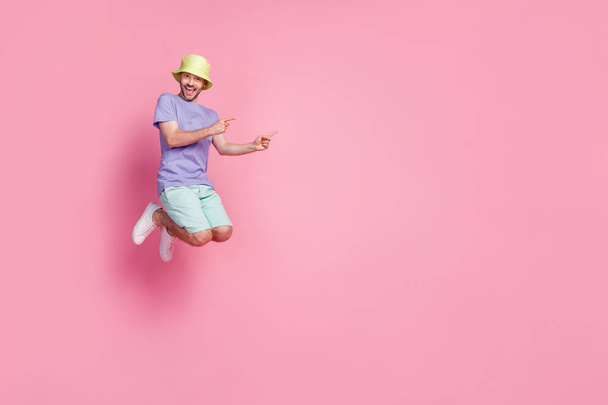 Full size photo of nice young man jumping pointing empty space enjoy pool party wear stylish blue clothes isolated on pink color background. - Foto, imagen
