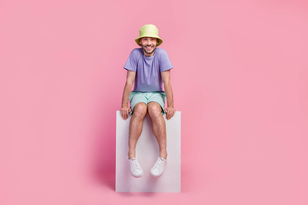 Full length photo of attractive young man sitting copyspace toothy smiling wear stylish blue outfit isolated on pink color background. - Fotoğraf, Görsel