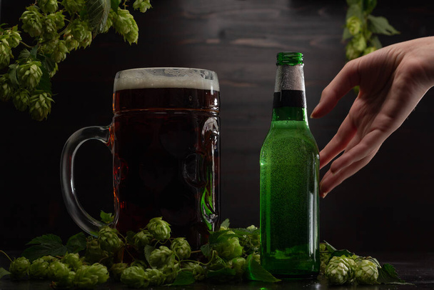 naisten käsi tarttuu olutpulloon ja lasilliseen olutta humalan taustaa vasten  - Valokuva, kuva