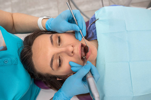Крупним планом фотографію красивої жінки оглядає стоматолог з стоматологічними інструментами в стоматологічному кріслі. Лікар лікує зуби пацієнта в кабінеті стоматолога
. - Фото, зображення
