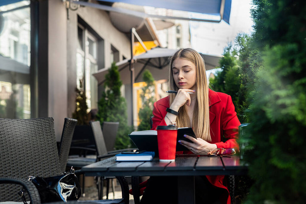 A beautiful blonde with charming hair has breakfast in a cafe using a laptop. Business concept - Fotografie, Obrázek