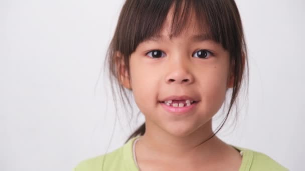 Retrato de una chica asiática con dientes de bebé superiores rotos y primeros dientes permanentes. Niña amigable mostrando sus dientes rotos aislados sobre fondo blanco. - Metraje, vídeo
