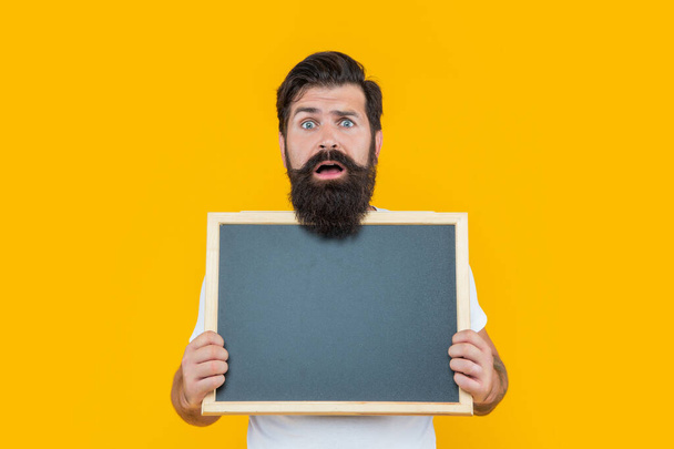 shocked bearded man with advertisement blackboard isolated on yellow. bearded man hold blackboard for advertisement. studio advertisement of man. man at advertisement blackboard with copy space. - Fotografie, Obrázek
