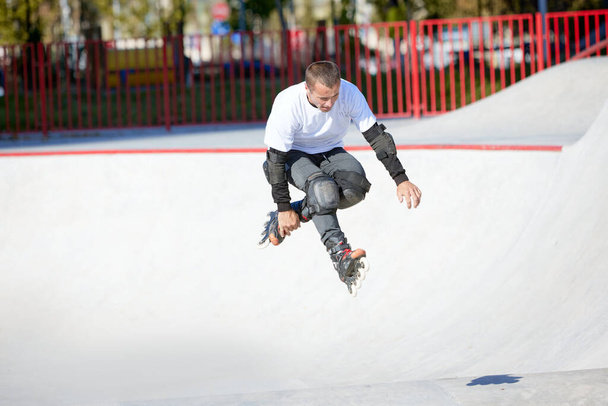 Mature male inline roller training in public skate park. Man practicing jumps, tricks. Concept of active lifestyle, sport, motion, hobbies. Leisure activities outdoors in autumn sunny day - Foto, imagen