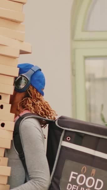 Vidéo verticale : Un livreur inconscient lâche des boîtes à pizza, un messager effrayé court depuis la porte d'entrée du client. Employé afro-américain maladroit livrant de la nourriture rapide, mauvais service de livraison, ayant peur - Séquence, vidéo