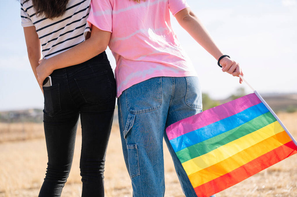Due amiche lesbiche schiena a schiena con una bandiera LGBT orgoglio. - Foto, immagini